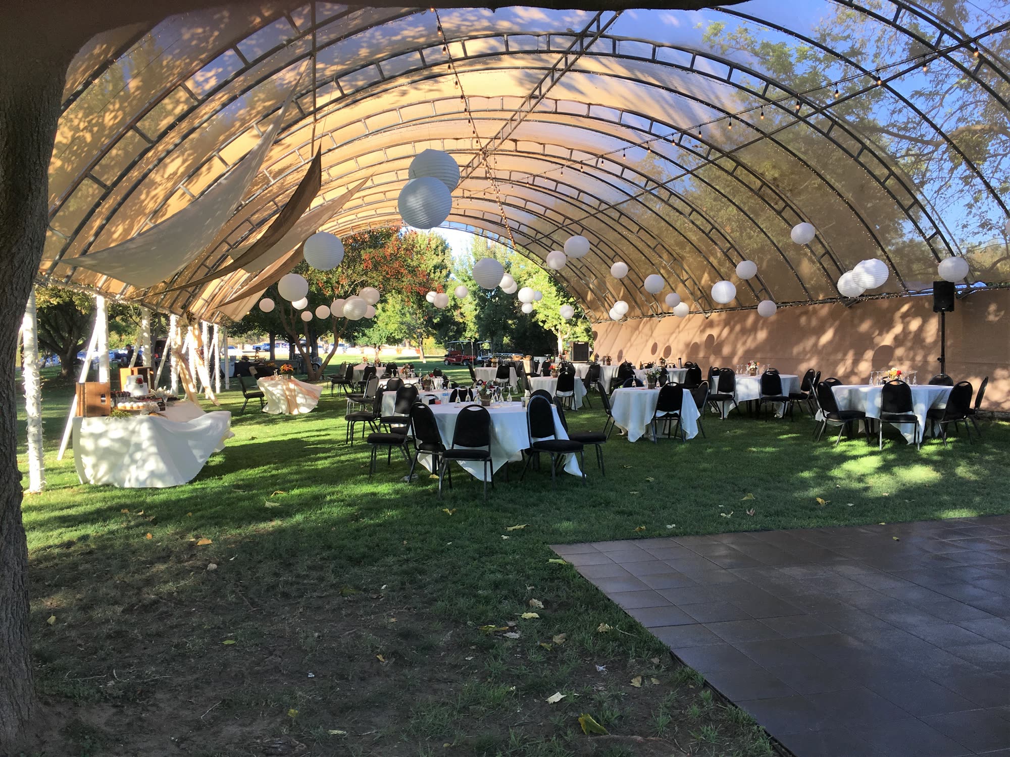 Reception tables set beneath the arched shade canopy with paper lanterns and string lights