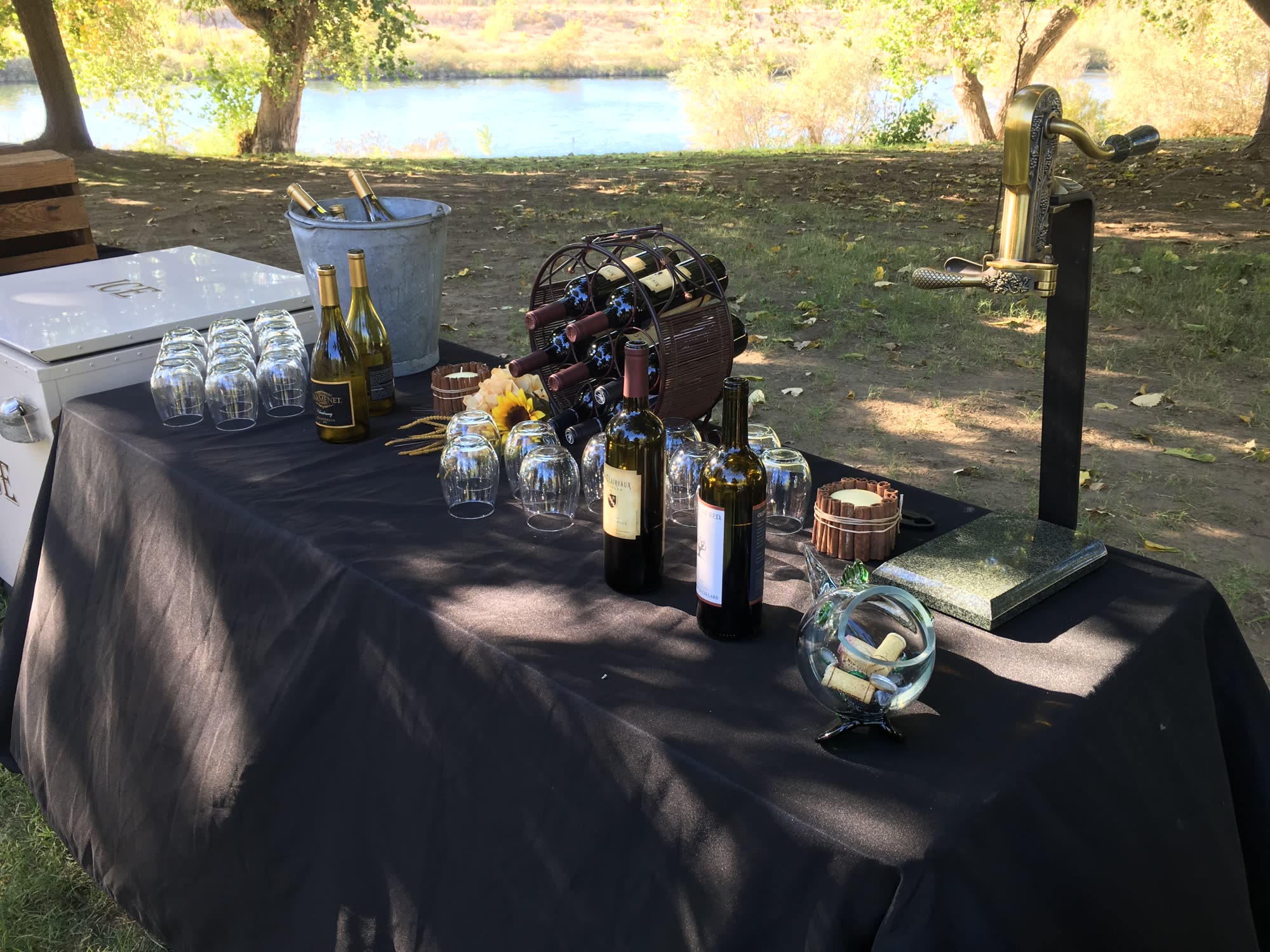Drinks table on the riverbank with wine, glassware and an ice chest under the trees