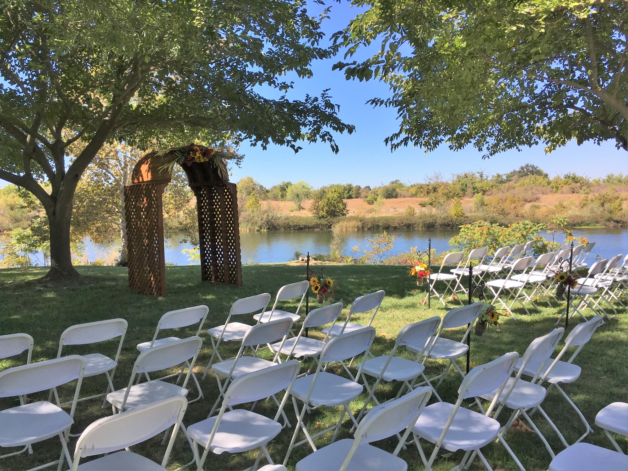 Rows of white chairs facing a flower-topped arbor on the lawn, the Feather River directly behind