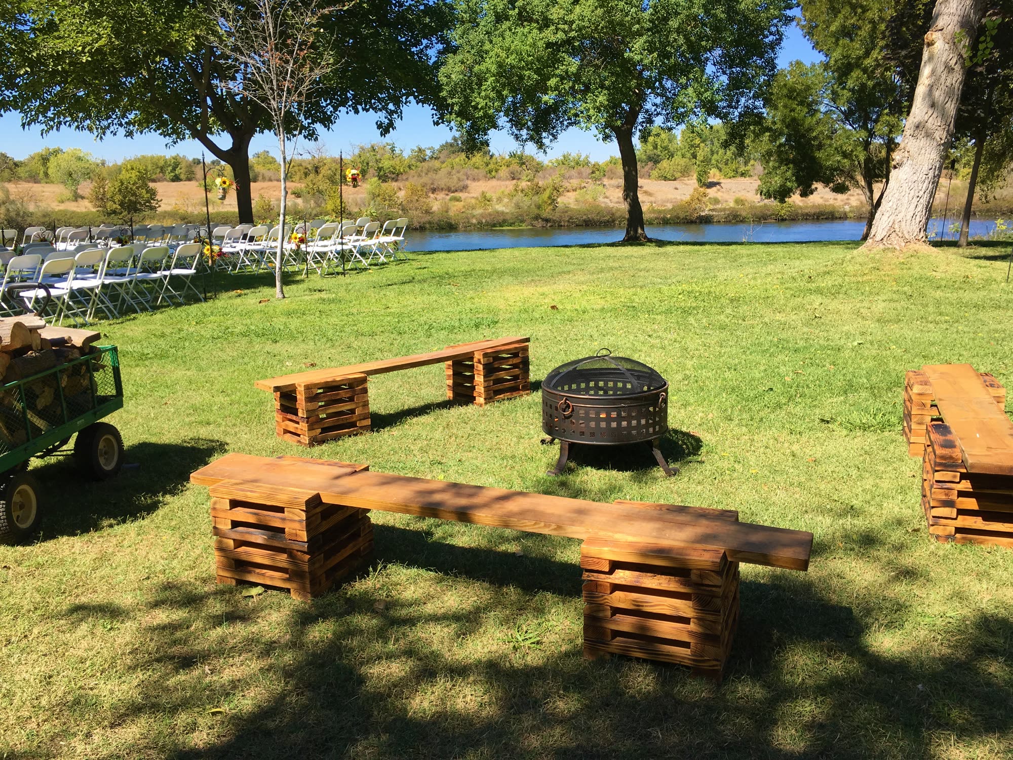 Timber benches around a fire pit on the lawn, with rows of ceremony chairs and the river beyond
