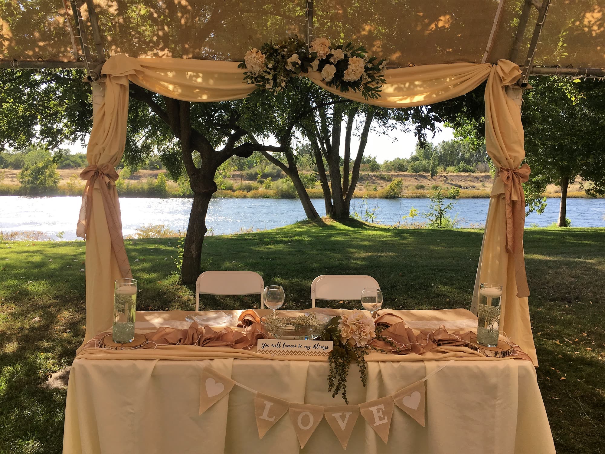 Sweetheart table draped in cream and blush linen under a canopy, the river beyond